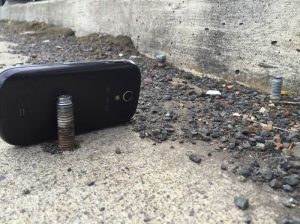 A bolt protruding from a road, close to the curb with a phone used to give scale