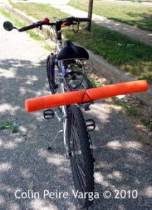 A bright orange noodle tied across the back of a bicycle